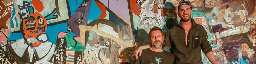 Two artists smile for a photo in front of their artwork